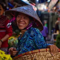 Laughing woman with a conical hat and a basket at a flower market