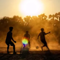 Boys playing football in dusty backlight