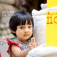 Little girl with a fringe next to rice sacks