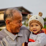 Grandfather laughing with a toddler in a bear hat in his arms