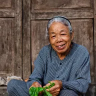 Old woman laughing with herbs in her hands in front of a wooden door