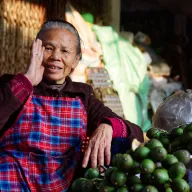 Elderly market woman behind green citrus fruit