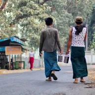 Two people in longyis walking along a road