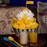 Mango shaved-ice dessert with cream, two small glasses beside it