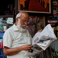 Elderly man reading a newspaper in front of his shop