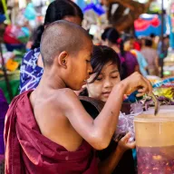 Young novice monk in a red robe at a market stall