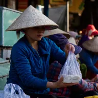 Market woman with a conical hat bagging rice cakes