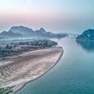 River with a sandbank between karst mountains, a bridge in the background, from above