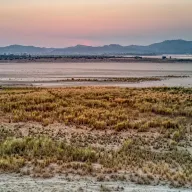 Dry riverbed with grasses at dusk, mountains on the horizon