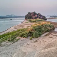Sandbank with grasses and an overgrown rocky island in the river