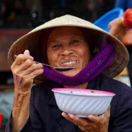 Old woman with a conical hat eating soup from a bowl
