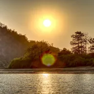 Sun above a river with a cliff and trees