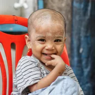 Laughing toddler with thanaka on a red chair