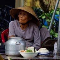 Old woman with a conical hat behind a teapot and bowls