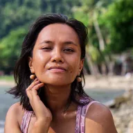 Young woman with earrings, hand on her cheek, beach in the background